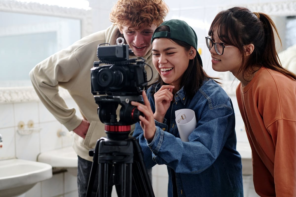 Group of three young people enthusiastically analyzing camera setup discussing project details and sharing ideas