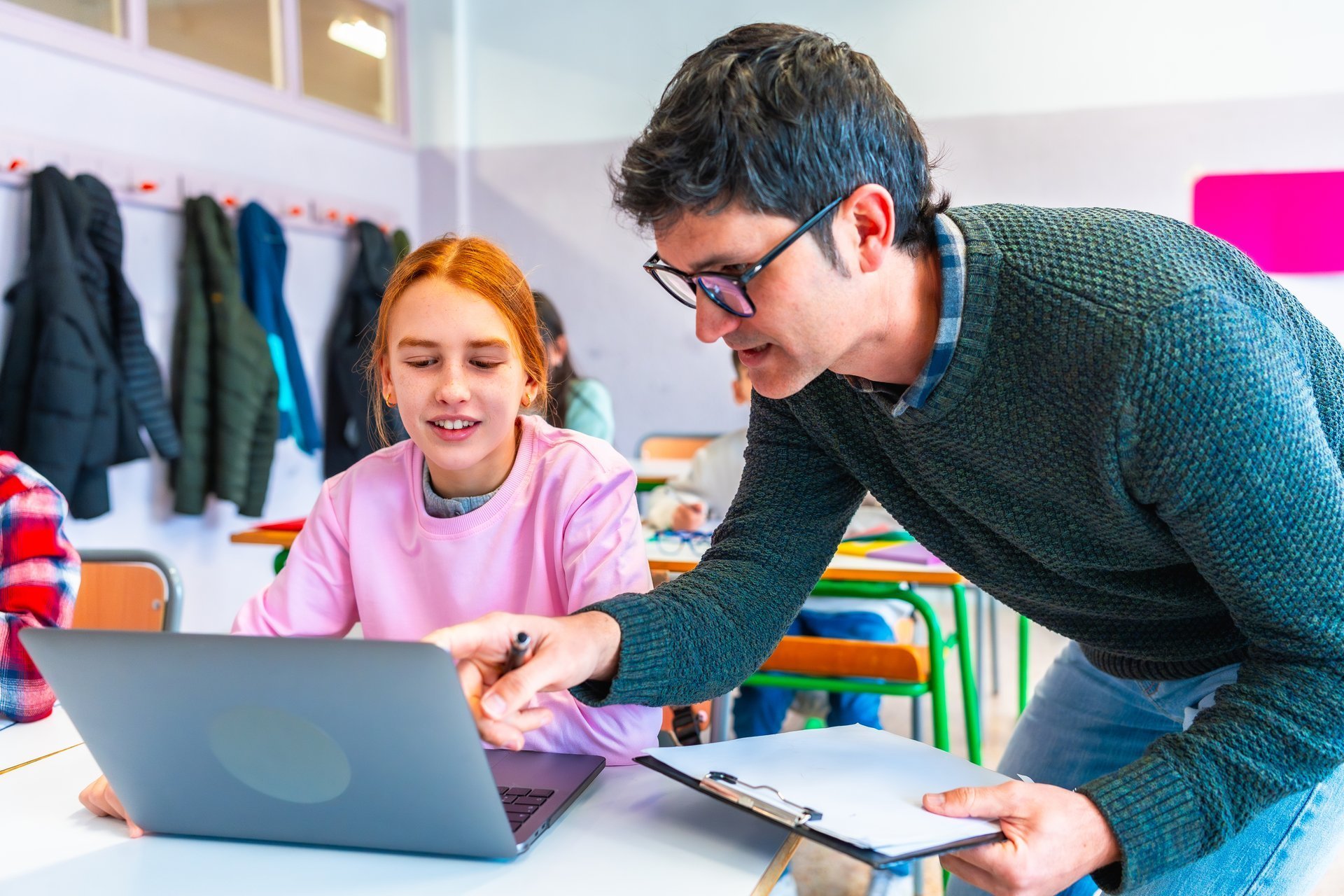 Teacher assisting a female student using a laptop during class, fostering a positive learning environment