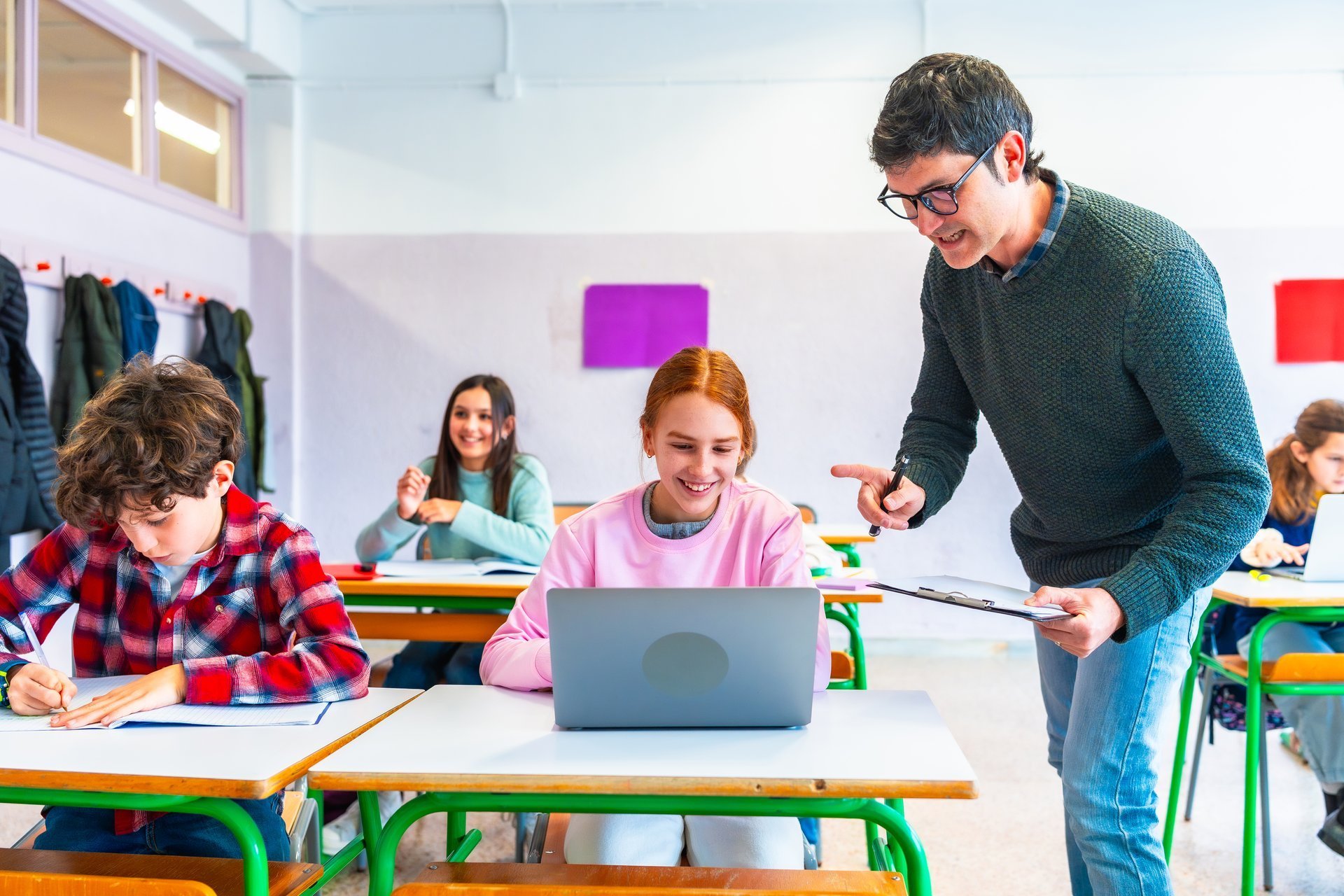 Teacher assisting students while studying with laptops in a vibrant classroom, fostering a collaborative learning environment