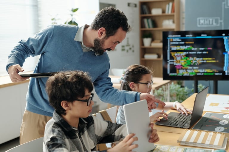 Teacher assisting students in learning programming in brightly lit classroom with open laptops