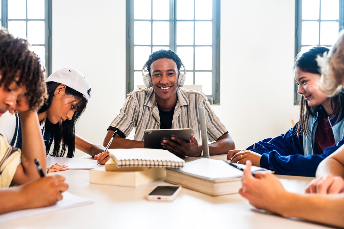 Multiethnic group of young students collaborating and using digital devices in a modern library classroom setting