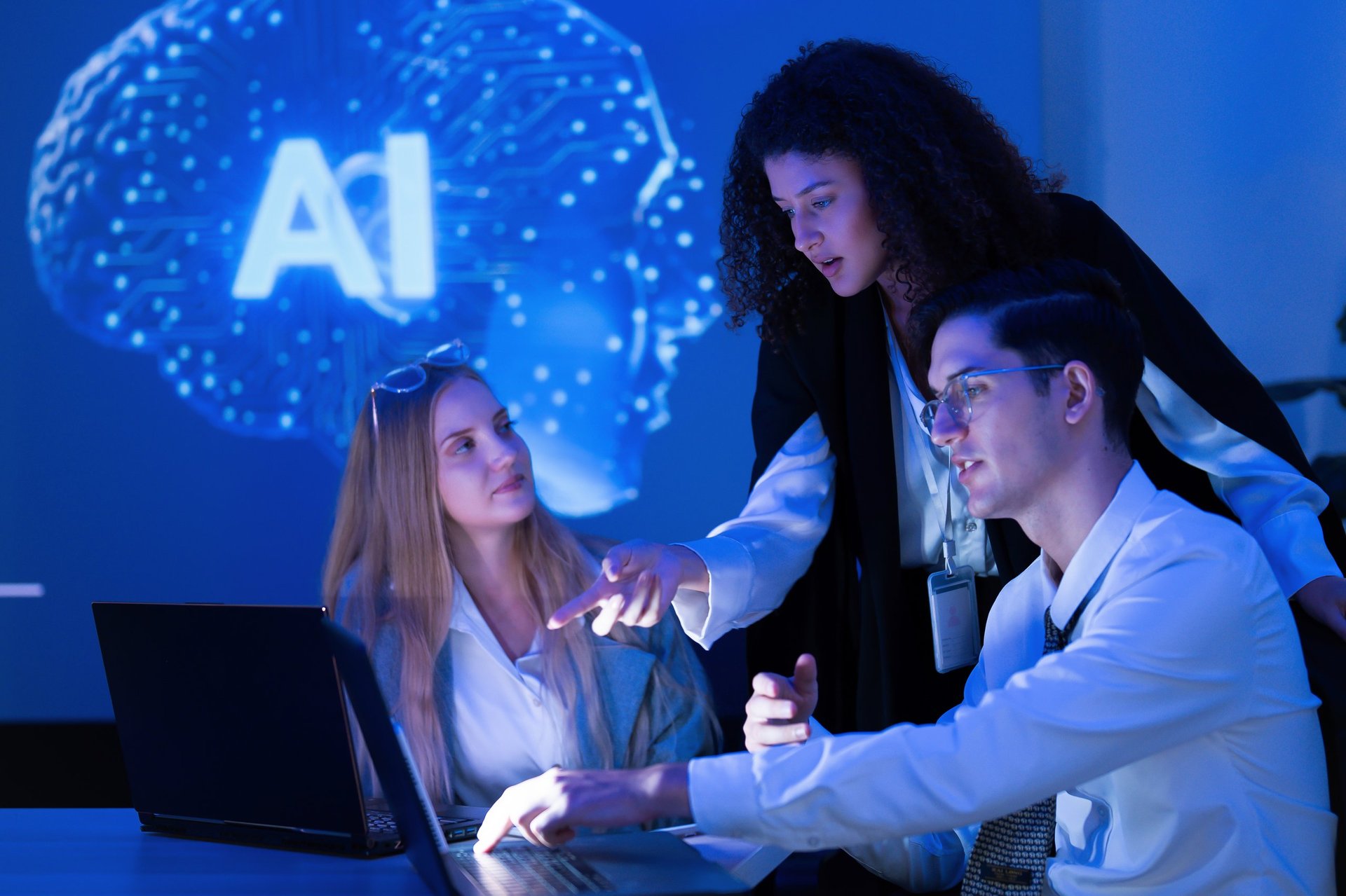 A group of three professionals engages in a discussion about an artificial intelligence project using a laptop in a contemporary setting with blue ambient lighting